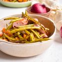Sheet pan sausages, sweet potatoes, green beans, and red onions in a bowl with spices.