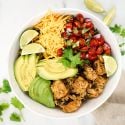 Slow cooker chicken burrito bowls with chicken breast, rice, black beans, avocado, and cheese in a bowl.