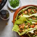 Slow cooker chicken lettuce wraps on a plate with lettuce leaves stuffed with chicken, mushrooms, peppers, and cilantro.