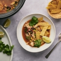 Slow cooker chicken tortilla soup with shredded chicken, beans, corn, cilantro, crispy tortilla strips, and lime wedges.