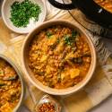 Overhead view of two bowls of creamy slow cooker Madras lentils with potatoes and spinach, garnished with fresh parsley and served beside a slow cooker.