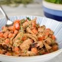 Slow cooker pork paprikash in a bowl with tomatoes and sour cream in a bowl.