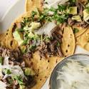 Shredded salsa verde beef served in corn tortillas, garnished with chopped onions, sauce, and fresh cilantro.