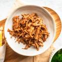 Slow cooker Italian beef in a bowl with shredded beef in a red sauce served with bread and spinach on the side.