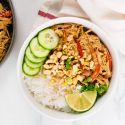 Slow Cooker Thai Peanut Chicken in a bowl with rice, cucumbers, chopped peanuts, and lime. 