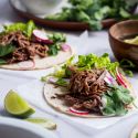 Slow cooker tri tip tacos on white corn tortillas with lettuce, cilantro, and radishes.