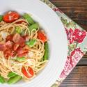 Snap pea pasta with bacon, cherry tomatoes, Parmesan cheese, and lemon in a white bowl.