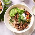 Southwest steak bowls with cooked steak, rice, black beans, cilantro, corn, pico de gallo, avocado, and sour cream.