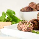 Spinach meatballs with lean beef and chopped spinach on a plate with tongs.