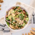 Spinach salad with creamy balsamic vinaigrette, goat cheese, apples, and walnuts in a white bowl with wooden salad tongs.