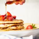 Strawberry Banana Oat Pancakes with maple syrup being poured on top.