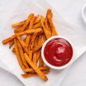 Baked sweet potato fries with a crispy exterior on a plate with ketchup.