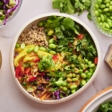 Thai bowls with quinoa, edamame, red bell pepper, kale, cilantro, and cabbage topped with peanut sauce.