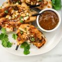 Thai peanut chicken skewers with green onions and peanut sauce on a plate.
