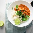 Thai red coconut curry chicken in a bowl with steamed rice, cilantro, basil, and fresh lime.