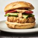 Tilapia fish burger with sauce cucumber and tomato on a sesame seed bun.