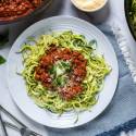 Tomato basil zucchini noodles with ground turkey served on a plate with basil and Parmesan cheese.