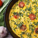 Baked frittata with tomatoes and goat cheese in a skillet with fresh herbs. 