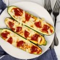 Zucchini pizza boats with marinara sauce, melted mozzarella cheese, and pepperoni on a white plate.