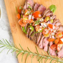Spanish steak with tomato salad on a cutting board with rosemary.