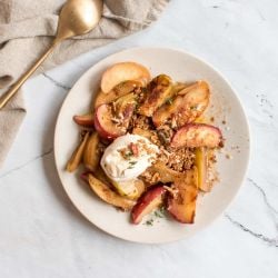 Grilled apples in a foil packet with cinnamon, yogurt, and granola on a plate.