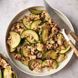 Bowl of ground turkey zucchini stir fry with tender zucchini slices and browned turkey, served with a knife and fork on the side.