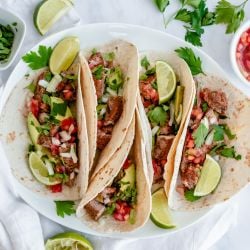 Steak tacos on flour tortillas with cilantro, onion, salsa, and lime.