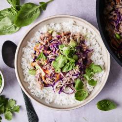 A bowl of white rice topped with sautéed ground meat, purple cabbage, and green herbs, beside a bowl of chopped scallions and fresh basil.