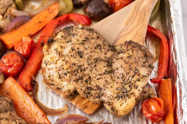 Roasted chicken thigh on a wooden spatula with vegetables.