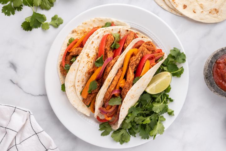 Chicken fajitas topped with peppers, onions, cilantro, and lime in flour tortillas.