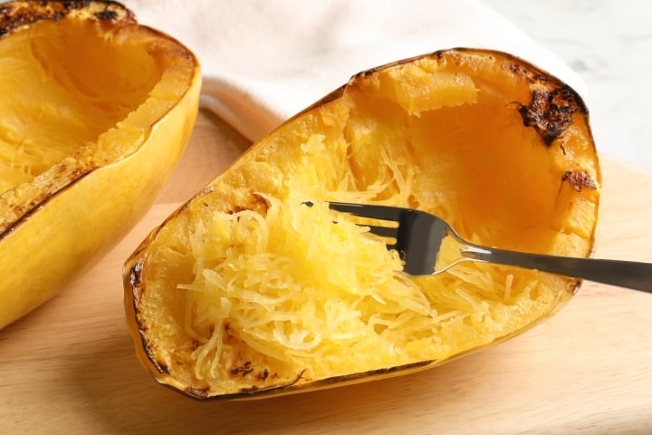 Roasted spaghetti squash on a cutting board with a fork scraping the squash into strands.