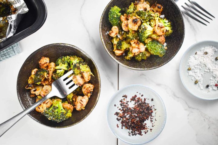 Roasted shrimp and broccoli in two bowls with Parmesan cheese and red pepper flakes.