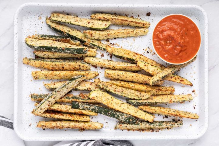 Low carb Parmesan zucchini fries on a baking dish with marinara sauce.