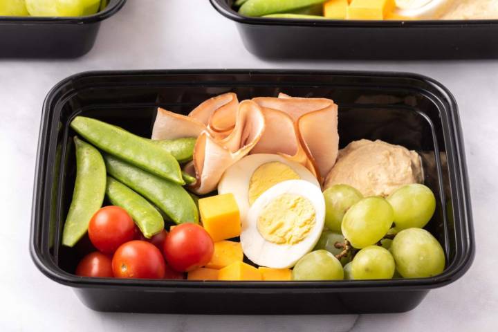 Healthy homemade bistro box with sugar snap peas, tomatoes, egg, turkey, cheese, hummus, and grapes.