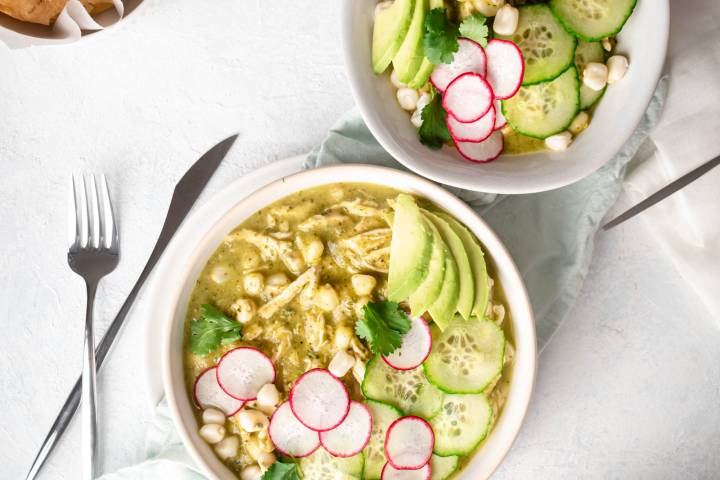 Green chicken pozole in a bowl with avocado, radish, cilantro, chicken, and hominy.