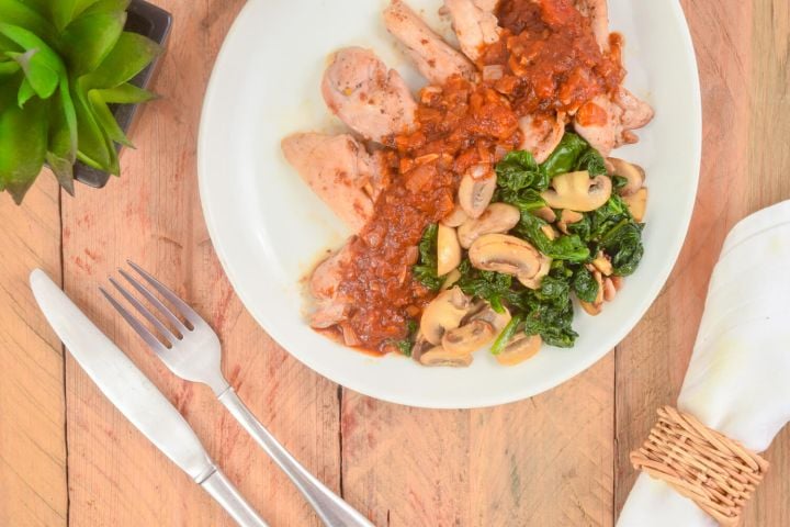 Balsamic chicken thighs with spinach and mushrooms on a plate with a napkin, fork, and knife.