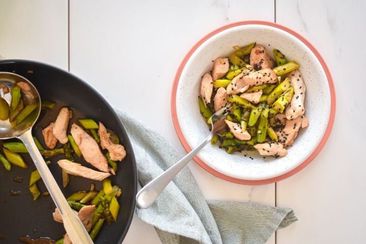 Chicken and asparagus stir fry with thinly sliced chicken breast, chopped asparagus, stir fry sauce, and sesame seeds in a bowl.