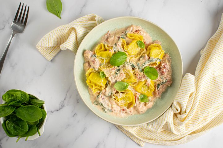 Creamy tortellini with tomatoes in a bowl with Parmesan cheese and basil.