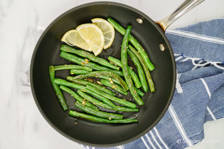 Garlic green beans in a skillet with fresh lemon slices.
