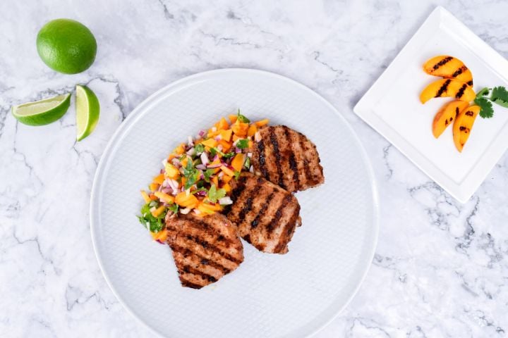 Grilled pork chops with peach salsa with fresh limes and peaches on the side.