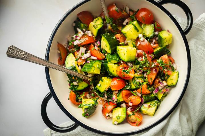Israeli salad with cucumbers, tomatoes, red onion, parsley, and lemon dressing in a bowl.