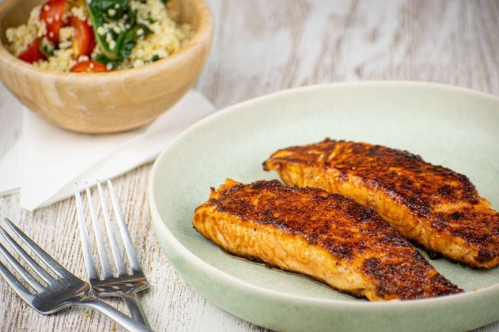 Sweet and spicy salmon with a spice crust on a plate with salad in the background.
