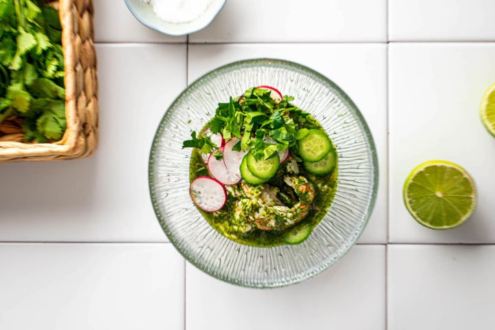 Aguachile with raw shrimp in a lime and cilantro sauce in a bowl with sliced cucumbers.