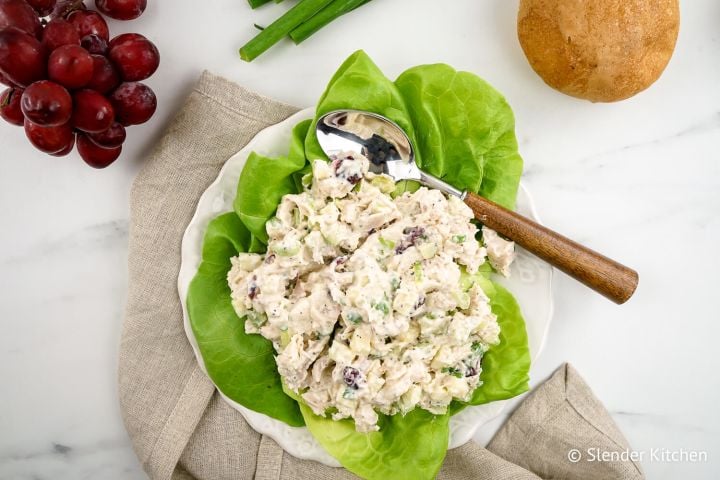 Cranberry chicken salad with apples in a white bowl with a spoon.