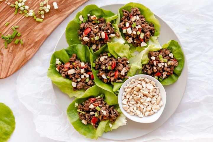 Asian ground beef lettuce wraps served on a plate with beef, mushrooms, peppers, and cashews wrapped in butter lettuce.
