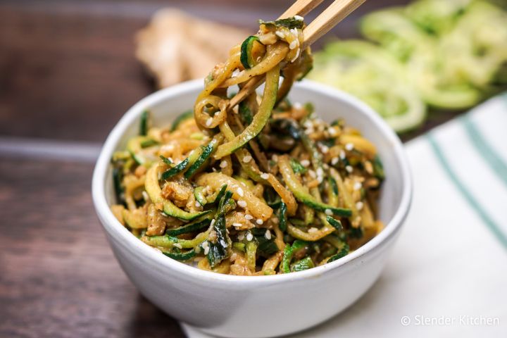 Asian zucchini noodles in a bowl with chopsticks lifting out a spoonful.