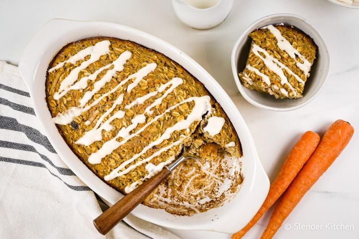 Baked carrot cake oatmeal with a cream cheese glaze in a baking dish with shredded coconut and oats.
