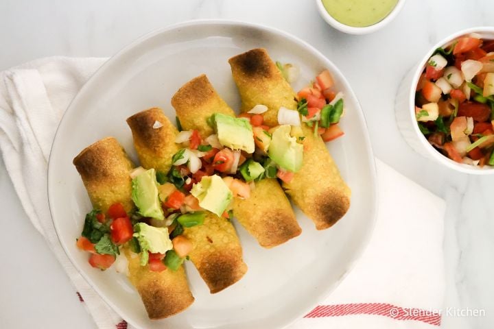 Chicken Taquitos on a plate with pico de gallo and avocado.
