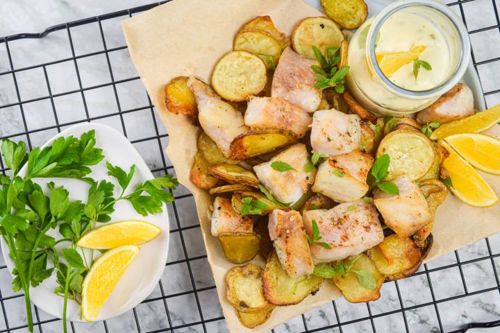 Baked fish and chips with crispy fish and potatoes on parchment paper with tarter sauce.