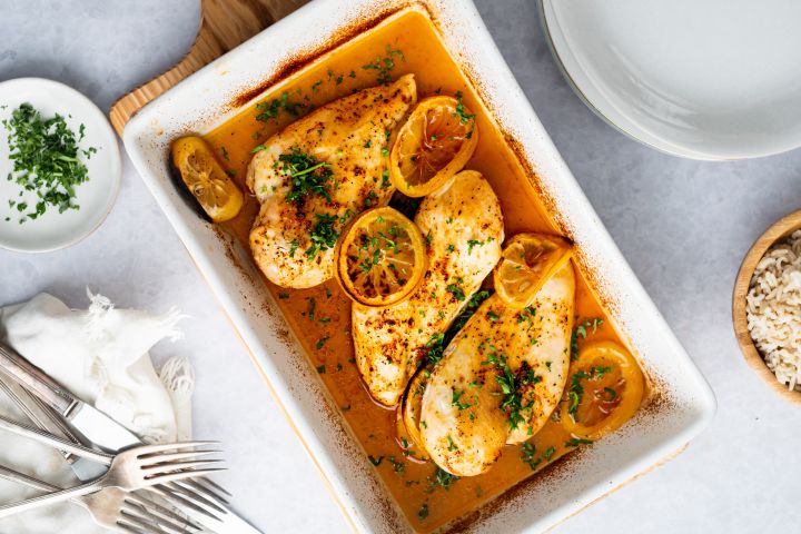 Baked lemon pepper chicken breasts in a baking dish with lemon slices and parsley. 